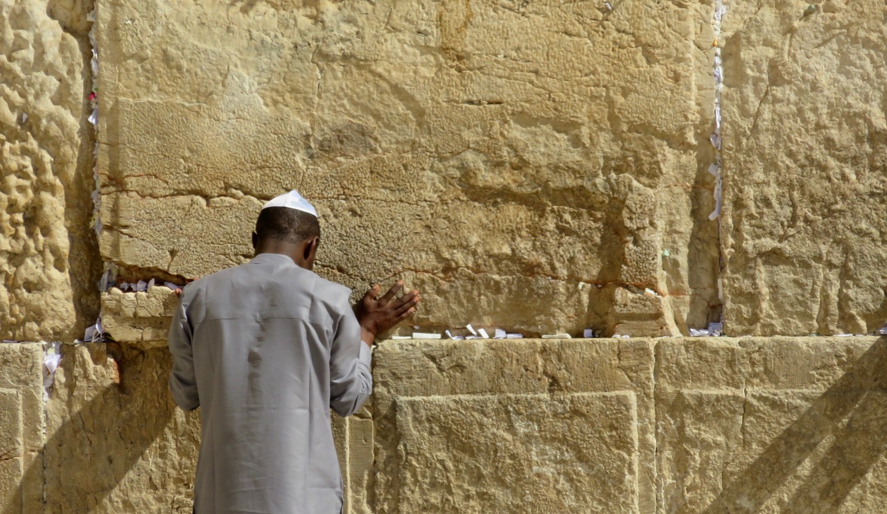 A pilgrim prays at the Wailing Wall, prayer messages all around him.